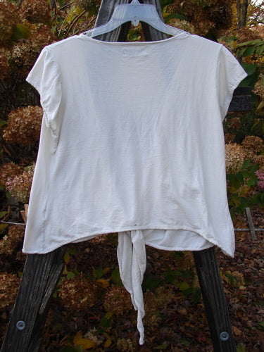 Barclay Cotton Lycra Cap Sleeve Tie Shrug Unpainted Creme Size 2 on a rack, showcasing a deep V-shaped neckline, front tie option, sectional straight panels, and cap sleeves.