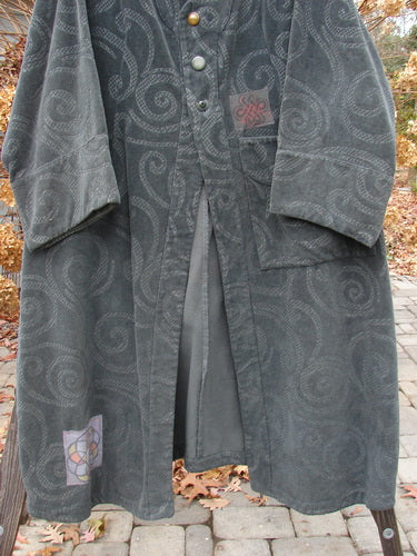2000 Patched Upholstery Diwmach Coat Swirl Black Size 2: A long grey coat on a wooden pole, accented with colorful patches and vintage buttons.