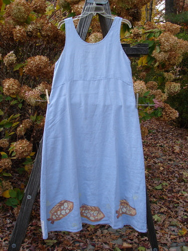 2000 Summer Shift Dress Fish Stream Size 1, displayed outdoors on a clothesline, showcasing its flowing linen fabric, downward curved empire waist, and bright hem with a spotted fish design.