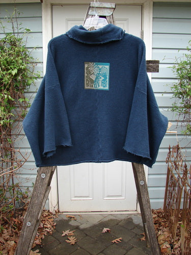 Barclay Patched Celtic Moss Crop Cowl Neck Pullover Navy OSFA displayed on a ladder, highlighting its floppy cowl neck, raw seams, and oversized crop fit with visible dolman sleeves and vented hem.