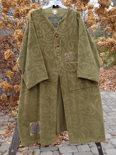 A 2000 Patched Upholstery Diwmach Coat Swirl Pine Size 2 displayed on a wood post, featuring a scalloped neckline, vintage buttons, colorful patches, and belled sleeves.