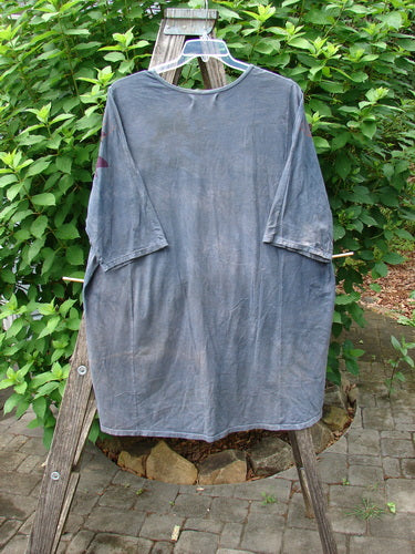 Barclay Tournesol Tunic Gull Flock Mottled Night Sky OSFA, featuring drop shoulders, loose three-quarter sleeves, a rounded neckline, and a varying hemline longer in the back, displayed on a wooden rack.