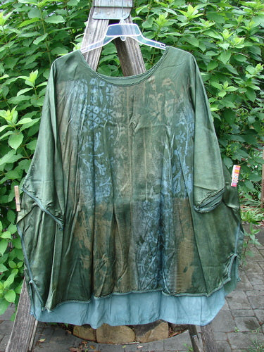 Barclay Viscose Vitreous High Low Tunic Botanicals Mottled Forest Sun OSFA hangs on a rack, showcasing its rounded neckline, varying hem, vented sides, and three-quarter dolman sleeves in a botanical theme.