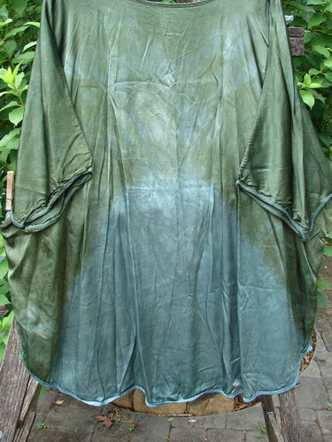 Barclay Viscose Vitreous High Low Tunic Botanicals Mottled Forest Sun OSFA, showcasing rounded neckline, varying hem, three-quarter dolman sleeves, exterior side stitchery, and botanical-themed shimmer on a clothes rack.