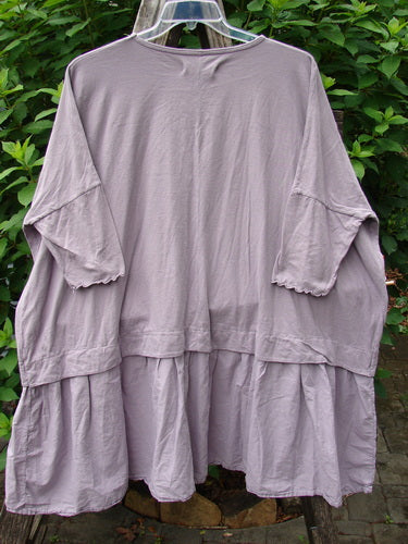 Barclay NWT Batiste Banded Flounce Esperanza Tunic Garden Sea Fog OSFA displayed on a hanger, showcasing its dolman sleeves, rounded neckline, batiste lower flutter, and unique floral theme paint.