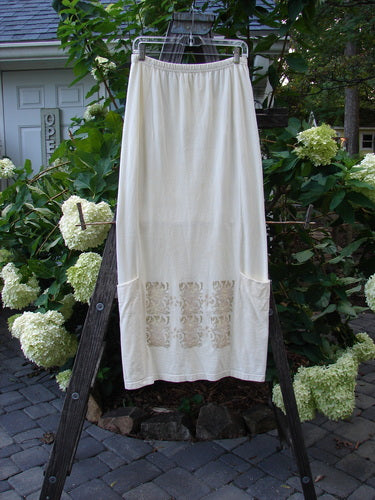 2000 Leaflet Skirt Garden Gates Milk Size 1 on a rack, featuring a slightly tapered hemline, billowy wrap-around sections, lower drop pockets, and a colorful garden gate theme painted on the front and back.