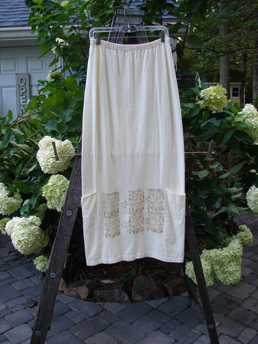 2000 Leaflet Skirt Garden Gates Milk Size 1 displayed on a wooden rack, featuring a dynamic hemline, wrap-around lower pockets, and detailed colorful garden gate theme paint on the front and back.