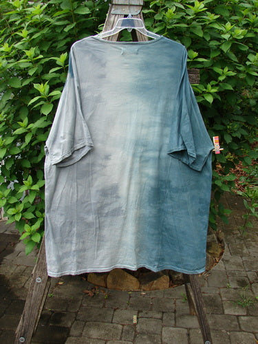 Barclay Art Tee Bud Rise Mottled Green Storm OSFA displayed outdoors, showcasing its longer tunic length, drop shoulders, loose three-quarter sleeves, and rounded neckline with floral-themed art.