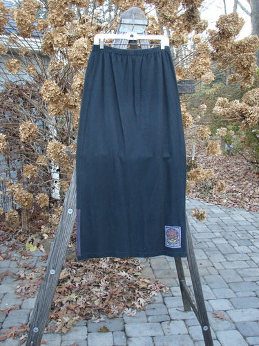 A long black skirt on a wooden rack, part of the 1999 Vented Straight Duo Heart Black Size 1 collection. Made from organic cotton, this skirt features a full elastic waistline and a colorful mosaic heart design. Perfect condition.