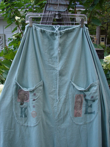 1994 Scoop Pocket Skirt Garden Fish Aloe Size 1, displayed on a clothesline, featuring a full drawstring waist, A-line shape, two front scooped pockets, and sectional panels.