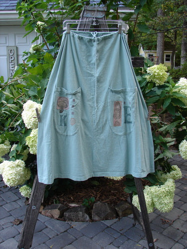 1994 Scoop Pocket Skirt Garden Fish Aloe Size 1 displayed on a clothes rack, featuring a drawstring waist, scooped painted pockets, and a sweeping A-line shape with vintage garden-themed panels.