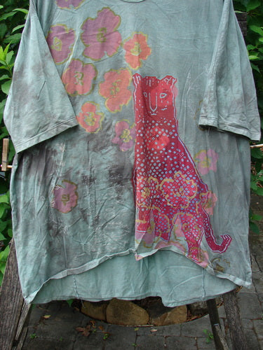Barclay Tournesol Tunic Spotted Cat Mottled Grass Field OSFA features a tunic-length design with drop shoulders and loose three-quarter sleeves. The pattern highlights a whimsical spotted cat theme amid side garden and village motifs.