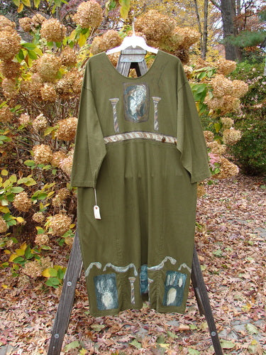 1993 NWT Holiday Button Maker's Dress Roman Goddess Olive OSFA displayed on a mannequin outdoors, featuring a deep V neckline, vintage buttons at the waist, and Roman Goddess-themed painting.