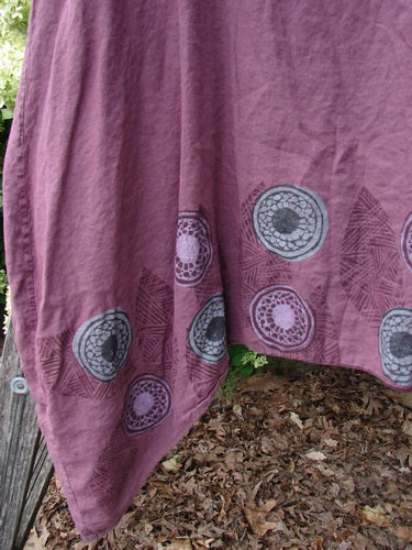 Barclay Linen Flared Pinafore Shift Dress, size 2, in berry linen with a soft drape and flared hem. The lower skirt shows pinwheel turn leaf medallions in gray and plum, set against a textured fabric with a muted, earthy finish.