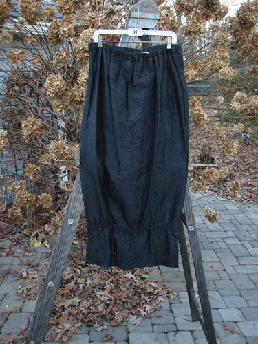 2000 Signed by Jen Shaunting Silk Gather Duo Spin Size 1: A black crushed silk skirt displayed on a wooden ladder, highlighting its full elastic waistline and unique pegged uptown look.