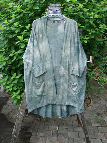 Barclay Bamboo Dolman Day Jacket Unpainted Mottled Field Grass OSFA displayed hanging outdoors, showcasing its open front, two drop pockets, cuffed sleeves, and unique hemline, reflecting BlueFishFinder's vintage style.