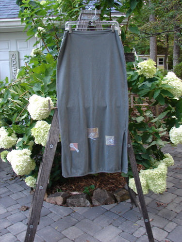 2001 Slim Skirt Junk Drawer Kelp Size 0 displayed on a wooden ladder, showcasing its flattering side vents and mid-bell shape against a garden backdrop.