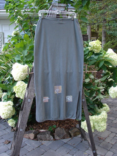 2001 Slim Skirt Junk Drawer Kelp Size 0 draped over a wooden ladder, showcasing its flattering mid bell shape and side vents, emphasizing its organic cotton and Lycra blend for a smooth fit.