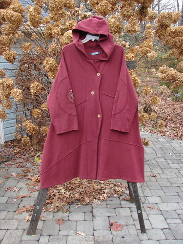 Barclay Patched Interlock Hooded Curve Coat on a rack, showcasing its cozy hood, painted patches, exterior stitching, and sweeping A-line flair.