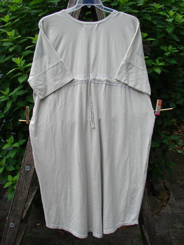Barclay Long Tee Tie Back Dress Botanical Garden Rain Cream OSFA displayed on a wooden rack, showcasing its seamless front, rounded neckline, drawcord back, and slightly short cuffed dolman sleeves.