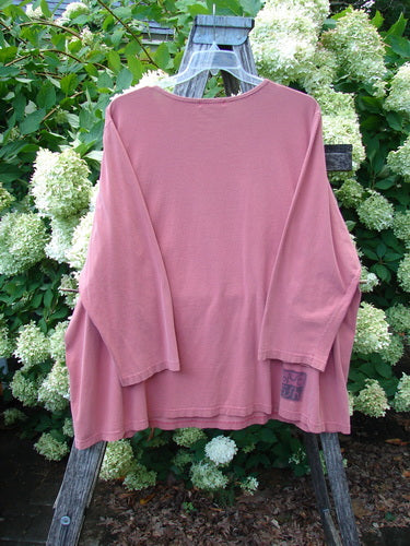 Barclay Long Sleeved Tee Studio Tee Triple Modernist in apricot, size 3, is a relaxed long-sleeve shirt with a soft matte knit and dropped shoulders. It hangs from a wooden easel against dense white hydrangeas and green foliage, with a small hem label visible near the lower right.