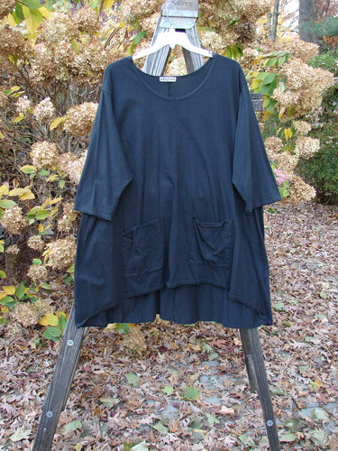 Barclay Hi Low Pocket Tunic Top Unpainted Black Size 2 displayed on a wooden stand, highlighting a soft neckline, varying hemline, A-line shape, and three-quarter sleeves with double lower exterior pockets.