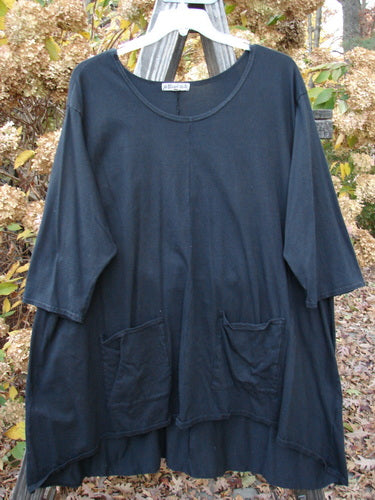 Barclay Hi Low Pocket Tunic Top Unpainted Black Size 2 displayed on a wooden hanger, showcasing a soft rounded neckline, varying hemline, three-quarter sleeves, and double front pockets.