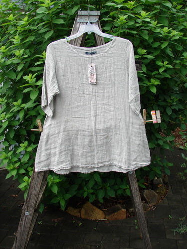 Barclay NWT Linen Springtime Top Unpainted Cloud Size 0 on a clothesline, showcasing its flowy A-line shape, rounded neckline, and almost three-quarter sleeves, emphasizing its lightweight linen fabric.