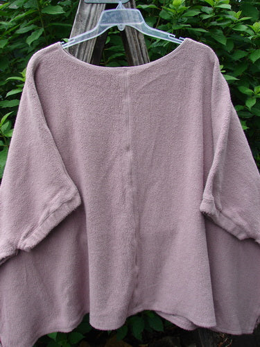 Barclay Celtic Moss Patched Poncho Single Flowerpot Mallow OSFA displayed on a wooden pole, showcasing its open sides, gathered lower sleeves, and dense textured feel, perfect for versatile styling.