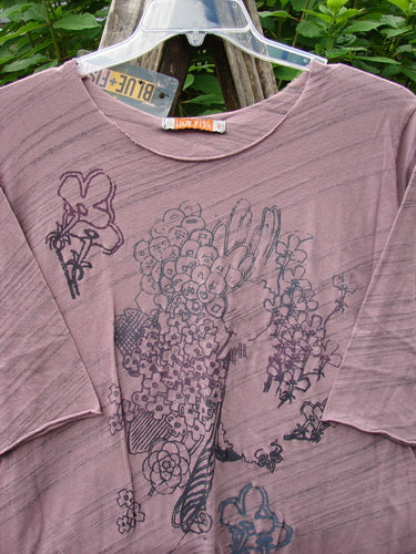 Barclay NWT Viscose Horizon Raw Cut Tee showcases a floral cluster and feather theme on a pink background. Features a raw cut neckline and three-quarter sleeves, reflecting BlueFishFinder's vintage style.