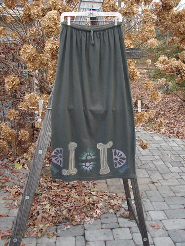 1993 Drawcord Skirt Column Black Sand Size 2: A long grey skirt on a wooden ladder, with a painted design.