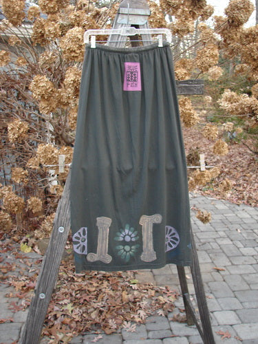1993 Drawcord Skirt Column Black Sand Size 2: A skirt on a wooden stand, featuring a full elastic and rope waistline. The skirt has a slight bottom flare and a blue fish signature patch.