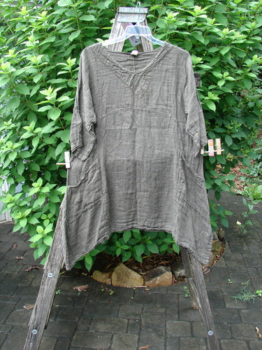 Barclay NWT Linen Cross Over Urchin Pocket Dress Unpainted Earth Size 1 displayed on a wooden rack, showcasing its smart cross-over V neckline, drop shoulders, and curved empire waist seam.