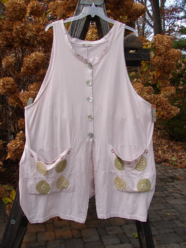 Barclay Shell Button Drop Pocket Vest in Pinwheel Pink Tile, displayed on a clothes rack, showcasing large front pockets, shell buttons, and a deep V neckline with a stand-up border.