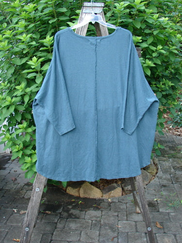 Barclay NWT Cotton Hemp Exterior Stitch Hi Low Tunic features dolman sleeves and a rounded neckline, displayed on a wooden stand. The tunic's botanical theme highlights its unique curvy stitchery and varying hemline design.