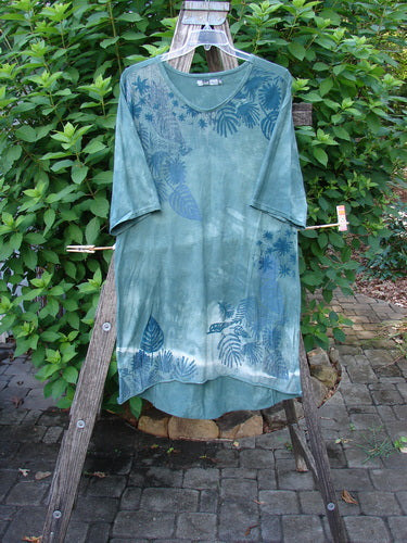 Barclay Tournesol Slim Tunic Beach Palm Mottled Green Earth OSFA displayed on a wooden ladder, showcasing its drop shoulders, loose three-quarter sleeves, and varying hemline with a beach palm theme.