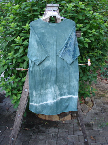 Barclay Tournesol Slim Tunic Beach Palm Mottled Green Earth OSFA, displayed on a clothes rack, features a longer tunic length, drop shoulders, three-quarter sleeves, and varying hemline.