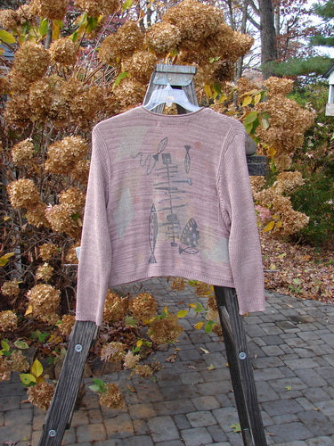 1995 Crop Cardigan Sweater Fish Space Twilight Rose Mélange OSFA displayed outdoors on a swing, showcasing its unique ceramic buttons, rolled neckline, and cozy long sleeves.