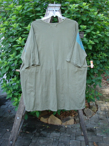 Barclay Tournesol Tunic Contour Forest Mottled Green Olive OSFA on a wooden rack, showcasing its loose three-quarter sleeves and rounded neckline, embodying BlueFishFinder's vintage, expressive style.