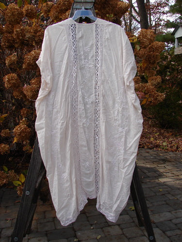 A Magnolia Pearl European Cotton Embroidered Lace Duster in Antique White, featuring an open flowing front, cap drop sleeves, gathered rear vertical lace seams, and a matching lace hem circumference.