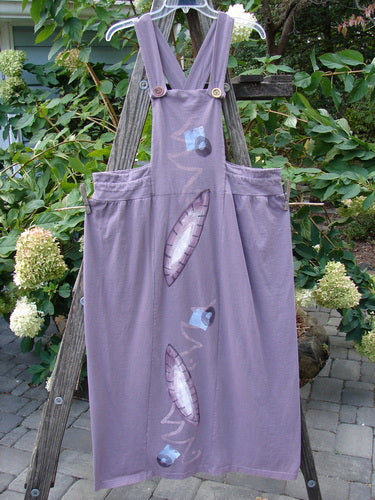 1996 Souvenir Jumper Turn Path Petunia Size OSFA displayed on a wooden ladder, featuring a painted bib, criss-cross back, gathered skirt, and drawcord back, highlighting its vintage, artistic design.
