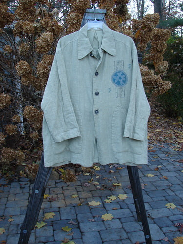 1999 Hemp Yard Coat Far East Cement Size 1 displayed on a hanger, featuring metal buttons, adjustable side tabs, and front pockets, showcasing its substantial weight and textured fabric.