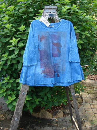 Barclay NWT Three Quarter Sleeved Cafe Tee Shadow Blend Mottled Blue Sky Size 0 displayed on a wooden rack, showcasing its unique A-line shape, rounded neckline, and curly edgings.