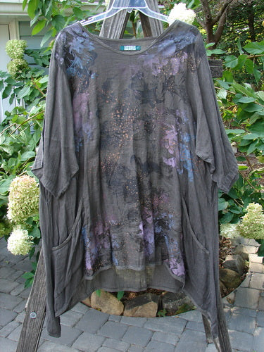Barclay Linen Drop Pocket Urchin Dress Continuous Bouquet Wood Size 2 on a clothes rack, showcasing purple and blue painted floral designs, rounded neckline, three-quarter sleeves, and exterior drop pockets.
