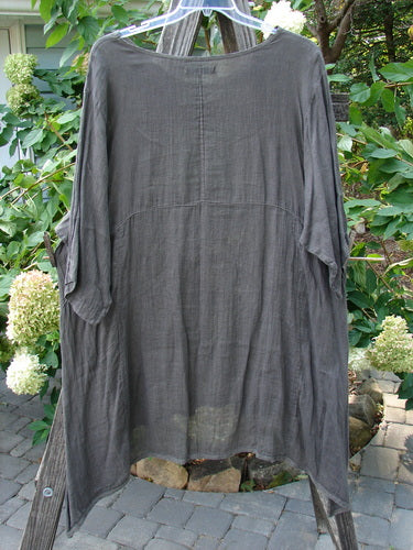 Barclay Linen Drop Pocket Urchin Dress Continuous Bouquet Wood Size 2 on a clothes rack, featuring a rounded neckline, three-quarter sleeves, exterior drop pockets, and a varying hemline.