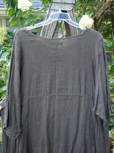 Barclay Linen Drop Pocket Urchin Dress Continuous Bouquet Wood Size 2 displayed on a hanger, showcasing its rounded neckline, three-quarter sleeves, and exterior drop pockets with a painted bouquet theme.