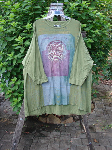 Barclay Art Tee Rose Script Mottled Peapod OSFA on a clothesline, featuring a tunic length, drop shoulders, loose three-quarter sleeves, and upward rounded front hem, highlighting its artistic design and generous sizing.