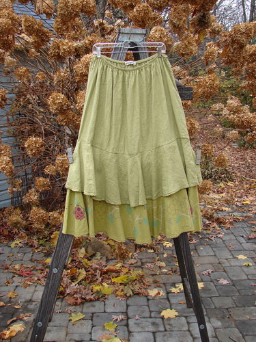 Barclay Linen Two Tier Ruffle Skirt Ladybug Yellow Olive Size 2 displayed on a rack, showcasing its elastic waistline, double A-line fall, and distinctive leaf-themed painted design.