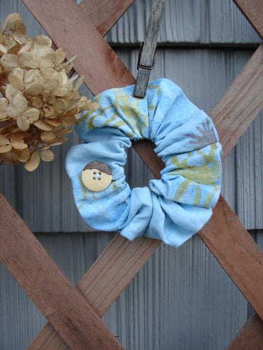 2000 PMU Linen Hemp Button Hair Scrunchie Abstract Sun Water Small displayed on a wooden surface, showcasing its ruffled fabric, thin elastic band, and decorative button, embodying sustainable vintage design.
