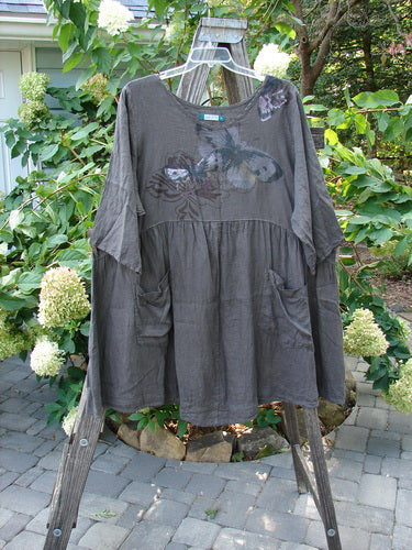 Barclay Linen Two Pocket Dolly Dress Butterfly Wood Size 2 displayed on a swing, featuring a flouncy lower skirt, dual exterior pockets, and a butterfly design on the upper bodice.